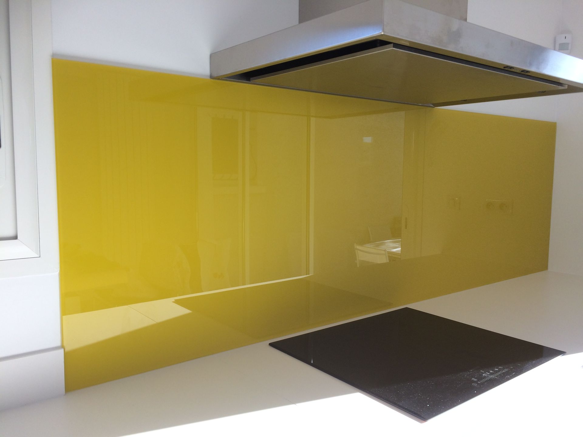 Crédence de cuisine jaune, plaque de cuisson noire et hotte en inox.