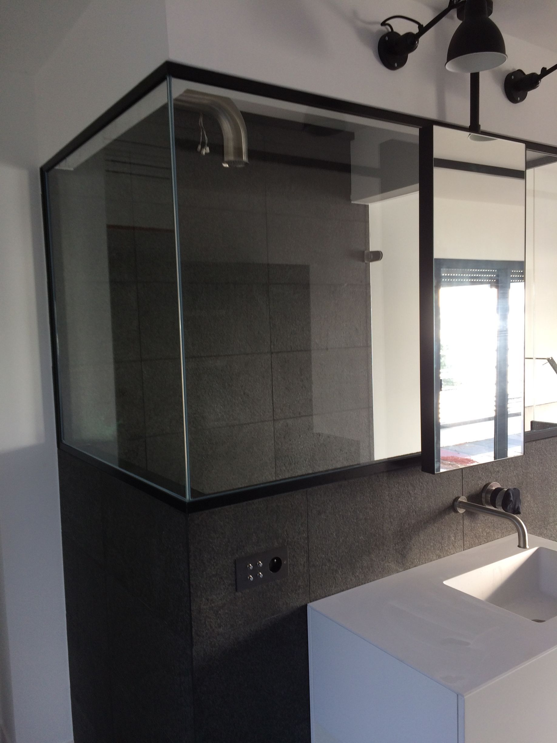 Salle de bains moderne avec douche vitrée, mur carrelé noir et plan de travail blanc pour le lavabo.