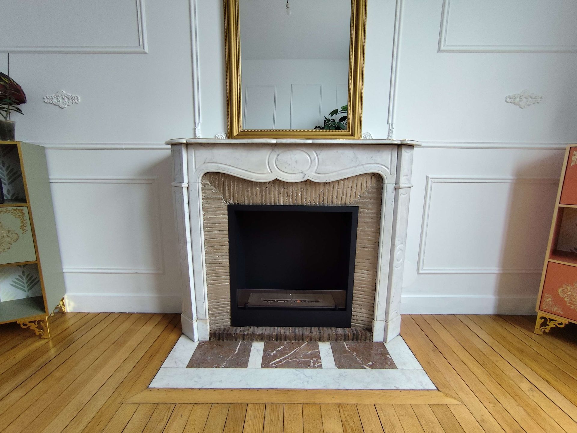 Poêle à bois noir moderne aux flammes orange dans une pièce minimaliste, posé sur un plancher en bois.