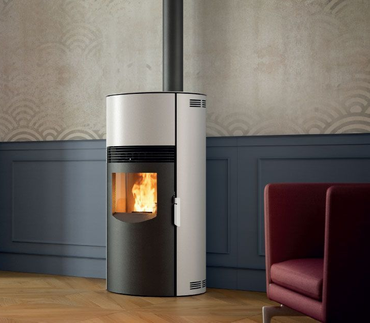 Poêle à granulés moderne blanc et noir avec un feu visible dans une pièce aux boiseries bleues et une chaise rouge.