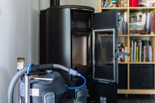 Poêle à bois, porte ouverte, se trouve à côté d'un aspirateur dans une pièce avec des étagères.