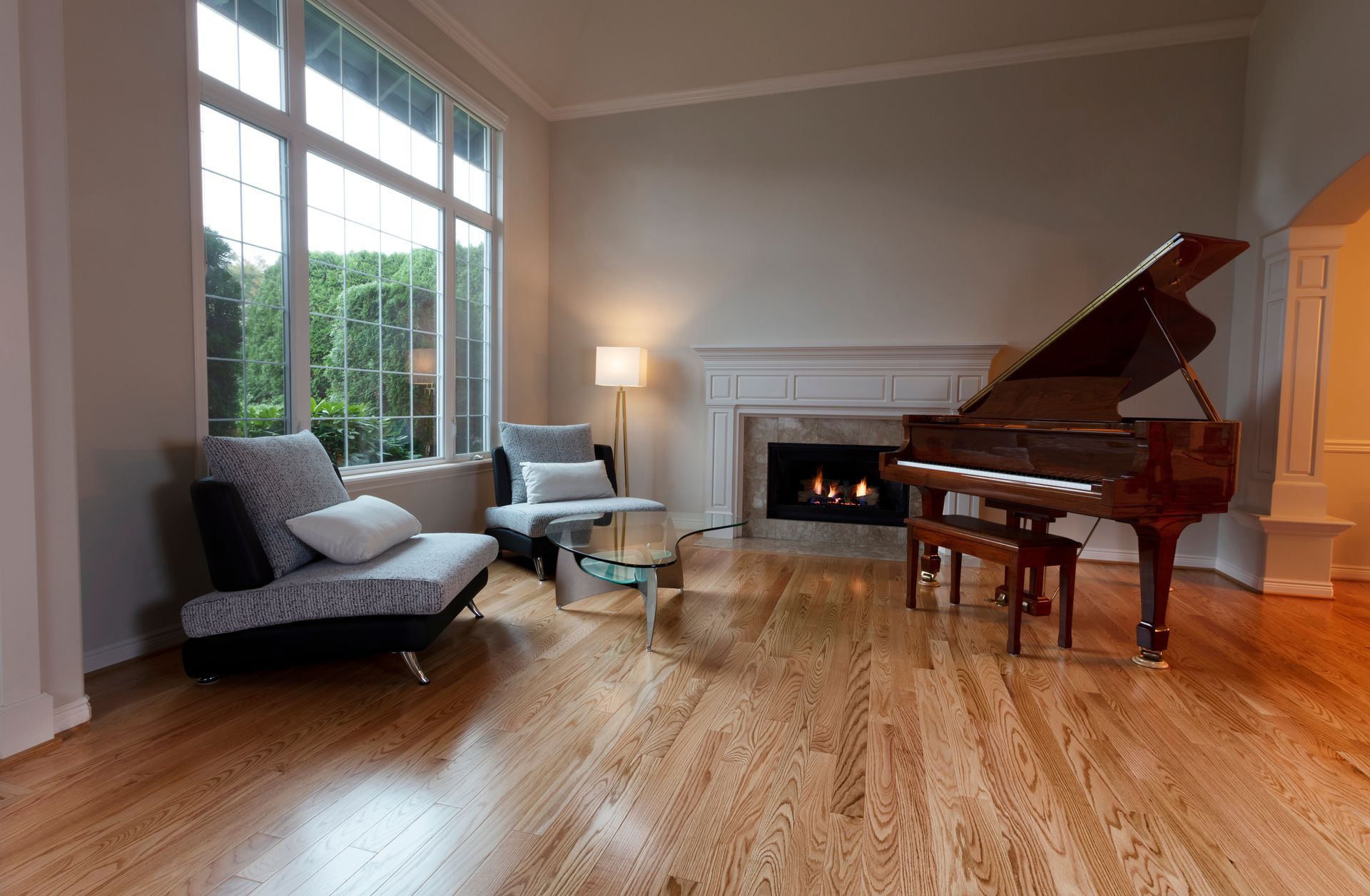 Salon avec piano à queue, cheminée, parquet et grande fenêtre donnant sur la verdure.
