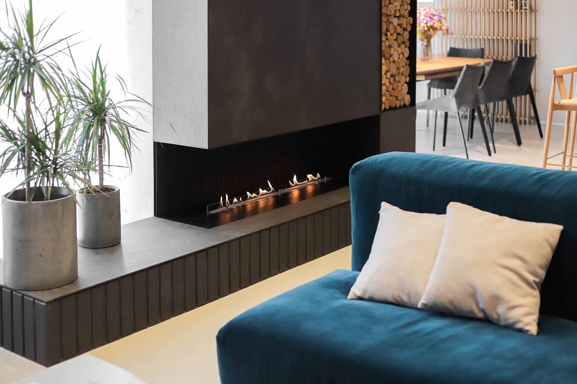 Salon moderne avec canapé bleu, cheminée intégrée et plantes en pot près de grandes fenêtres.