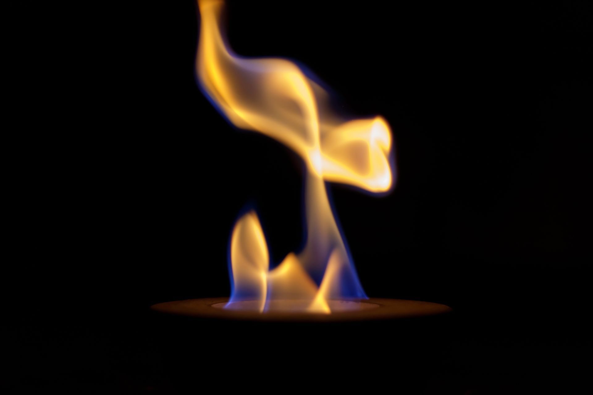 Une flamme orange s'élève d'un petit brûleur sur fond noir.