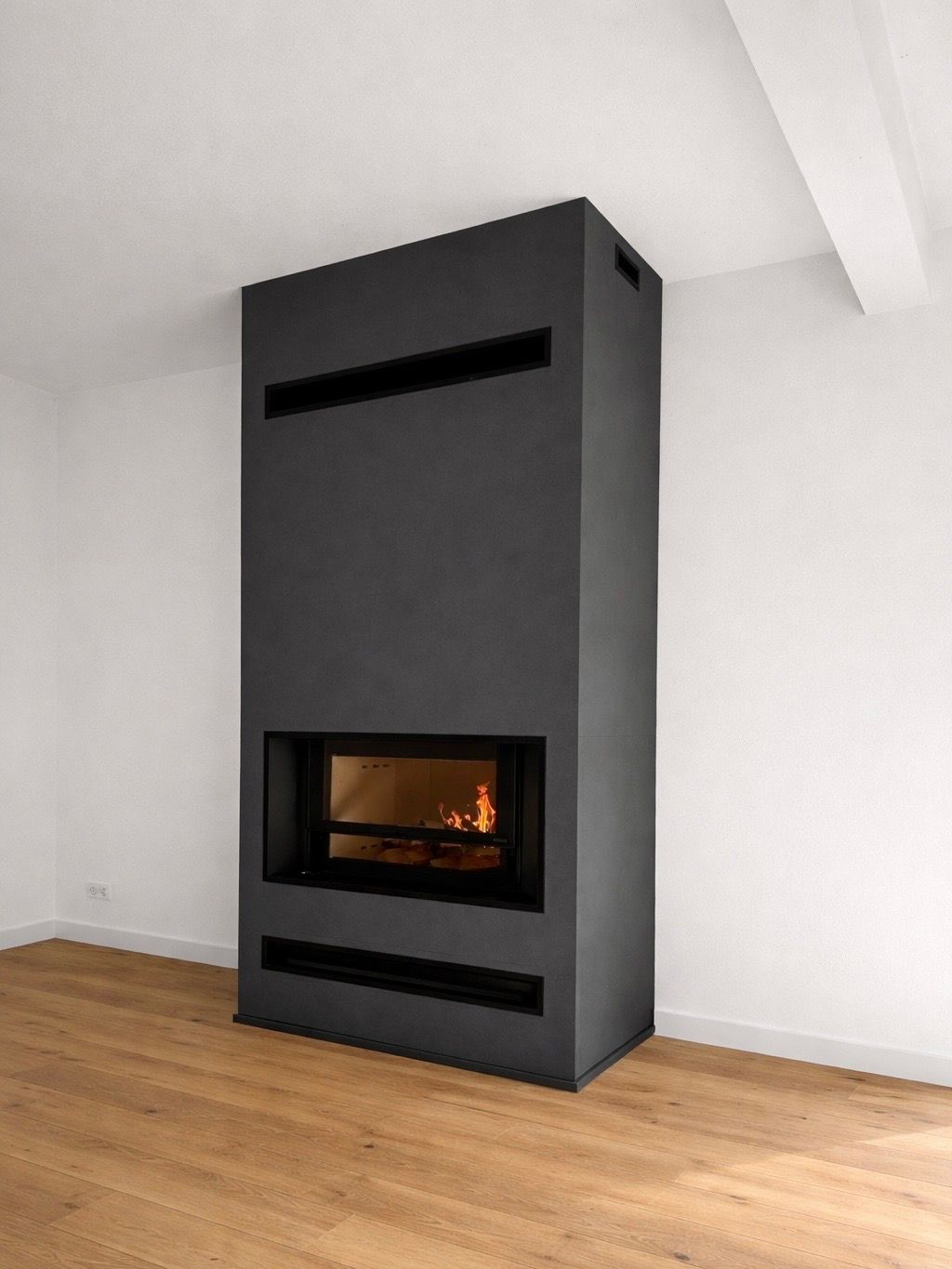 Salon moderne avec une cheminée cylindrique noire qui brille à côté d'un canapé et de grandes fenêtres.