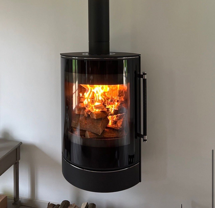 Poêle à bois noir moderne avec un feu qui brûle, encastré dans une niche murale avec des bûches empilées en dessous.