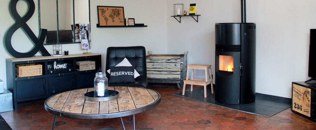 Salon moderne avec poêle à bois, meuble noir, table basse ronde et murs blancs.