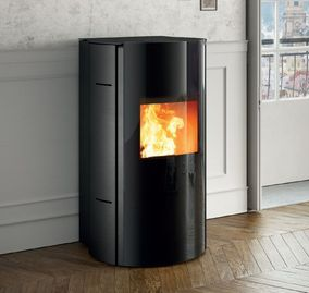 Poêle à granulés cylindrique noir avec un feu crépitant dans une pièce lumineuse près d'une fenêtre.