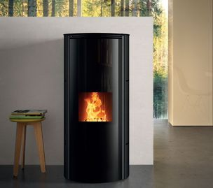 Poêle à granulés cylindrique noir avec flamme apparente dans une pièce moderne, à côté d'un petit tabouret.