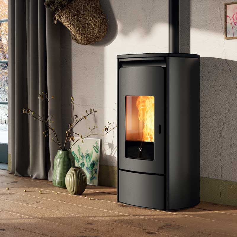 Poêle à granulés noir moderne avec flamme visible dans une pièce confortable près d'une fenêtre et de coussins de sol.