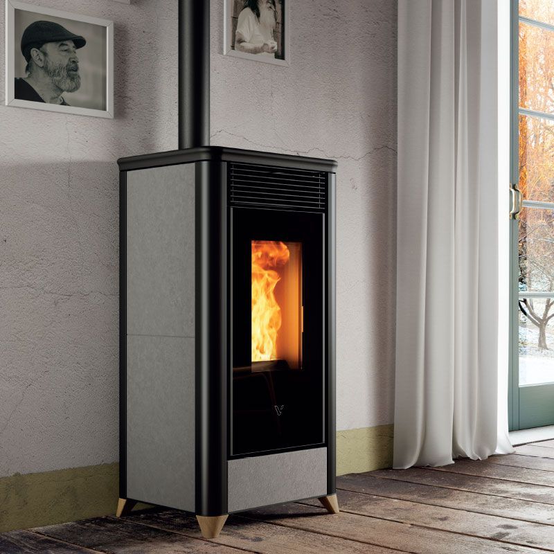 Poêle à granulés cylindrique noir avec flamme apparente dans une pièce moderne, à côté d'un petit tabouret.