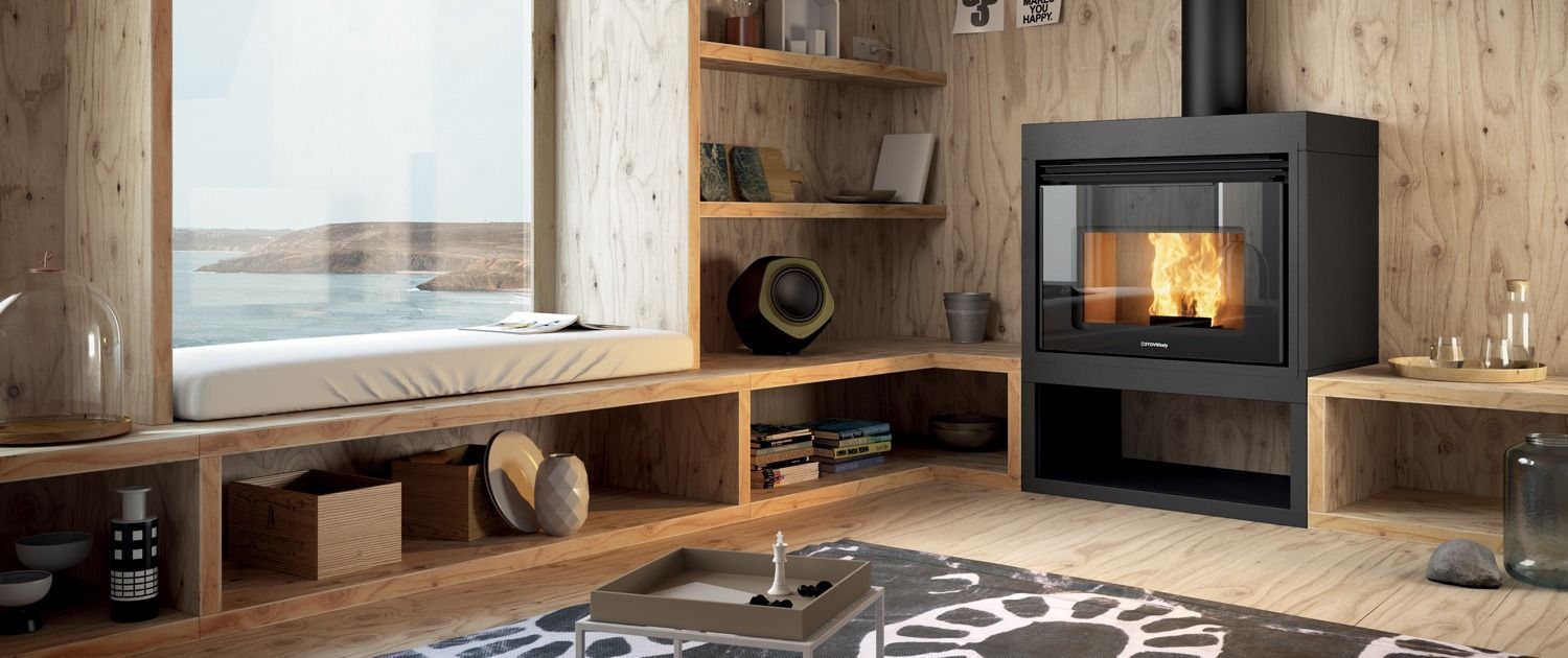 Salon chaleureux avec poêle à bois, grande fenêtre et étagères en bois intégrées.