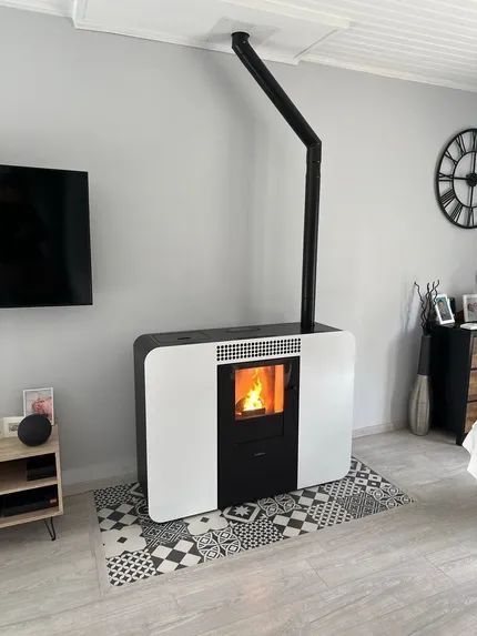 Poêle à granulés avec un feu allumé, conduit de cheminée noir et horloge murale dans un salon.