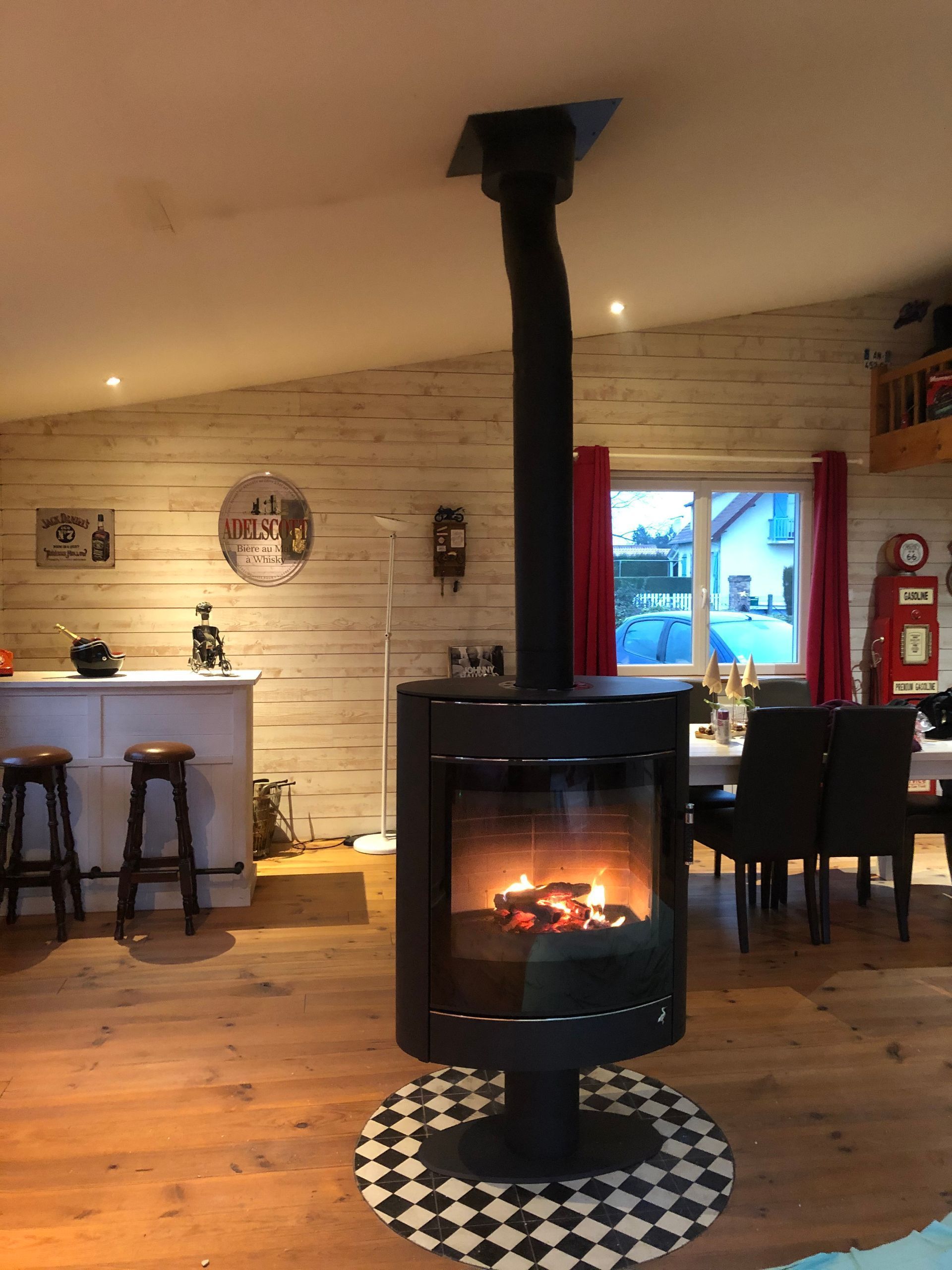 Intérieur de café chaleureux avec un poêle à bois noir placé au centre d'un tapis à carreaux.