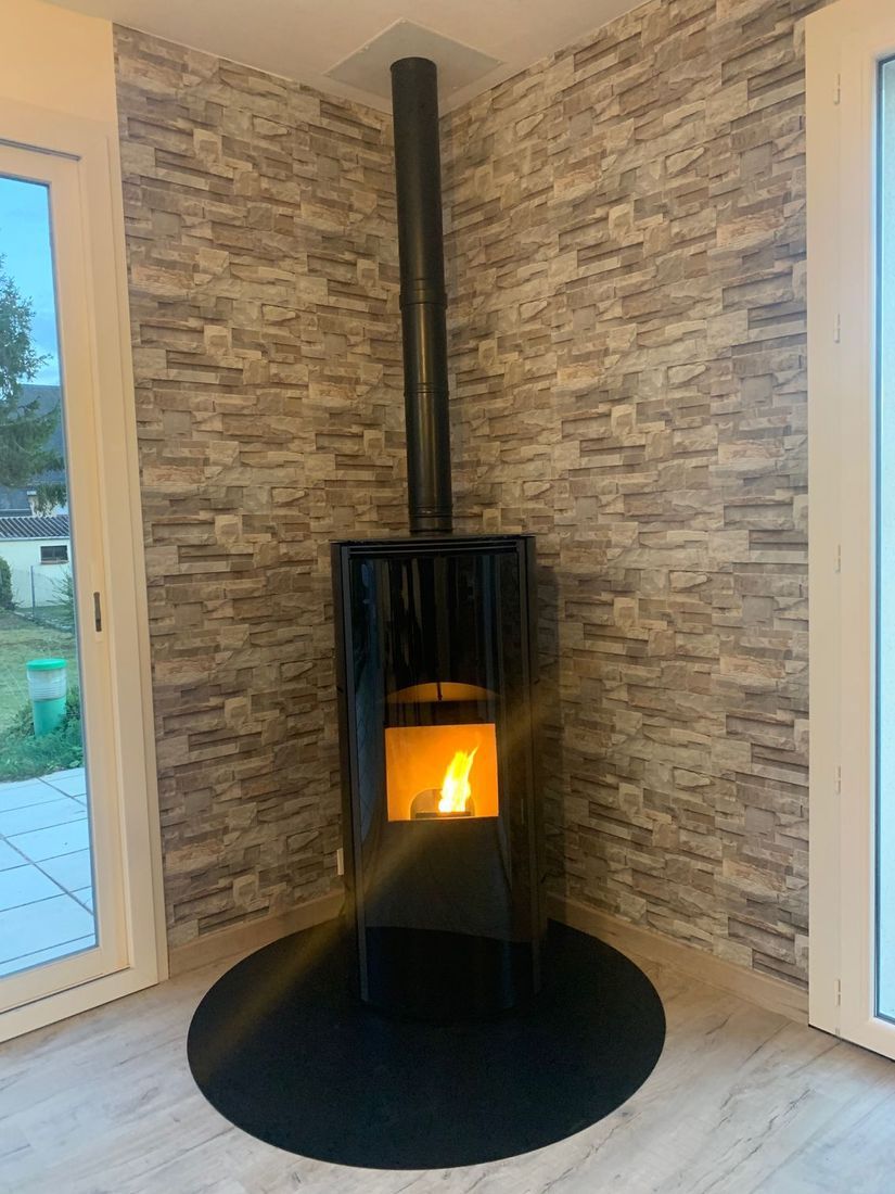 Poêle à bois noir avec un feu dans un coin, avec des murs en pierre et des portes vitrées des deux côtés.