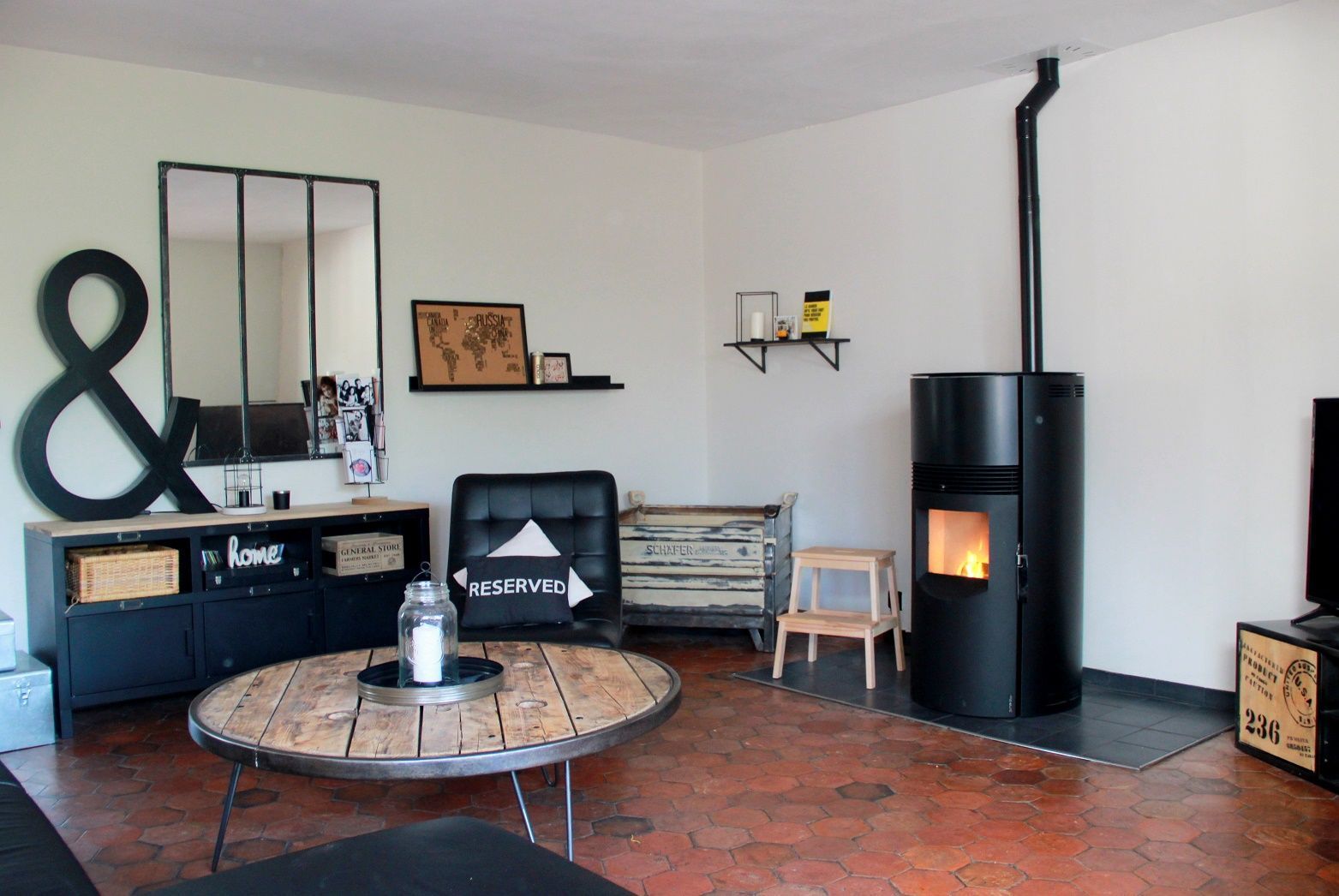 Salon moderne avec poêle à bois, meuble noir, table basse ronde et murs blancs.