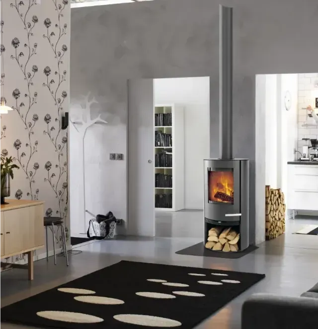 Salon moderne avec un tapis noir, du papier peint à motifs floraux et un poêle à bois près d'une porte.