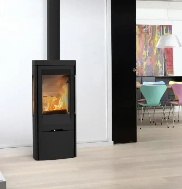 Poêle à bois noir à flamme visible dans une pièce moderne et lumineuse avec un coin repas attenant.
