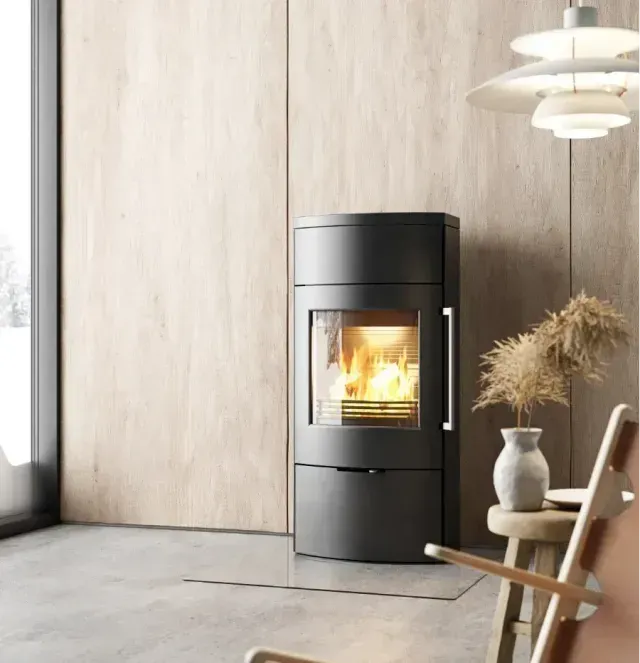 Poêle à bois noir moderne avec un feu qui brûle dans une pièce minimaliste aux bois clairs.