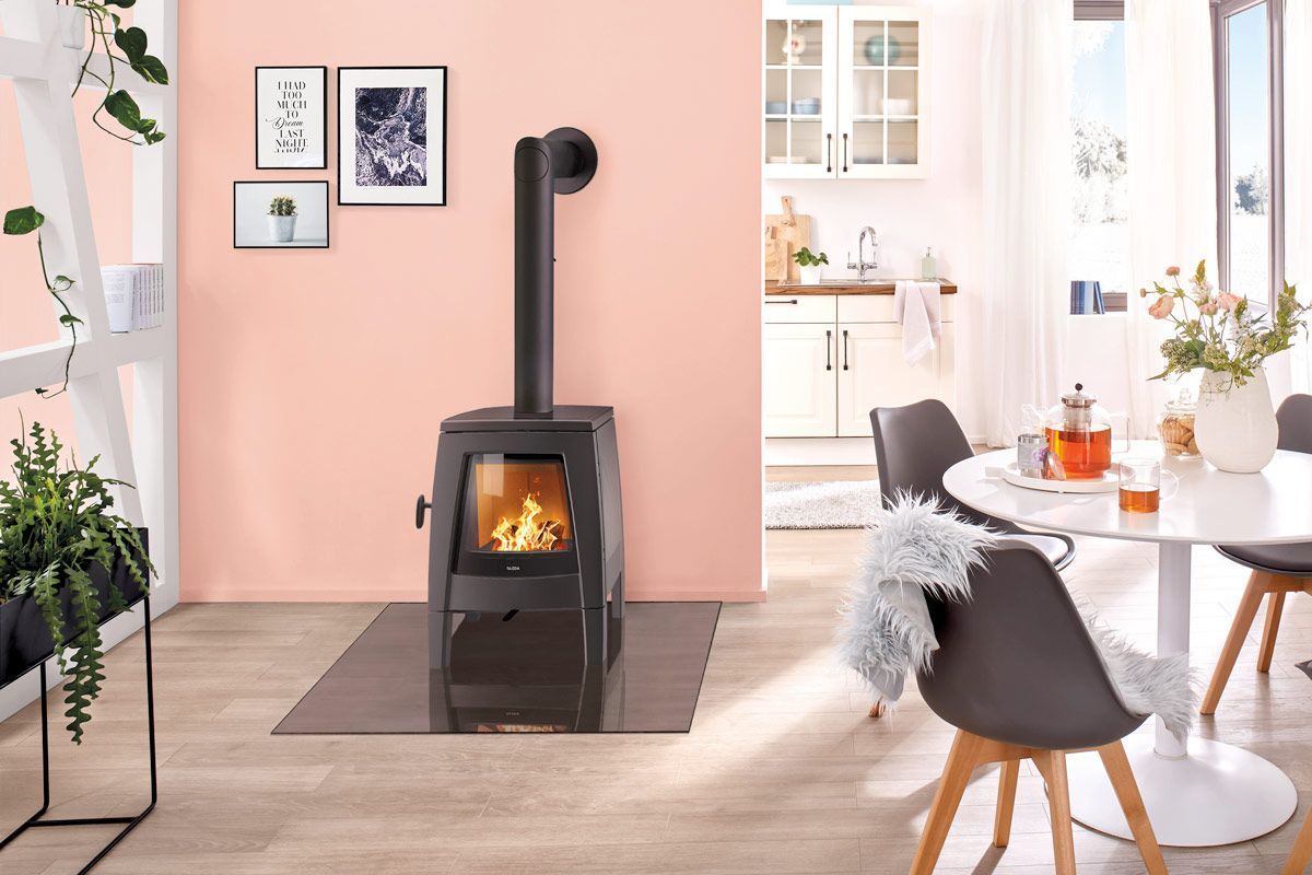 Salon chaleureux avec poêle à bois noir sur un mur rose, coin repas blanc et décoration moderne.