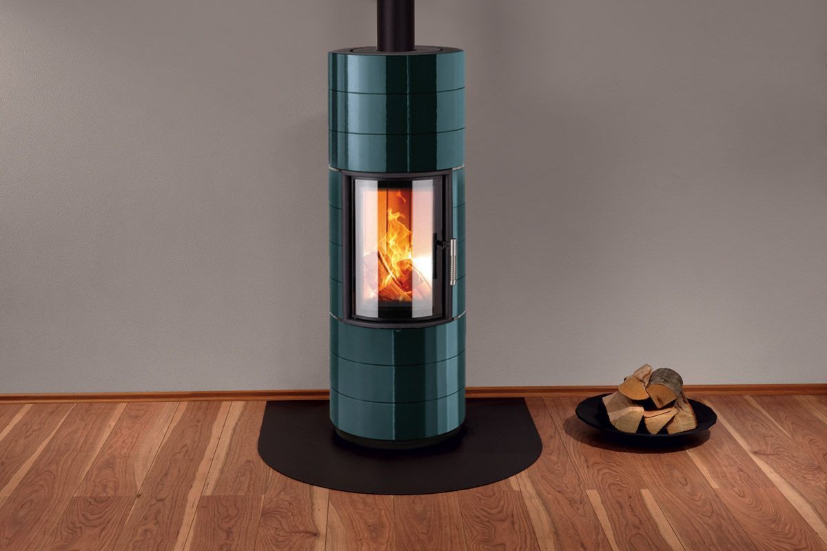 Poêle à bois cylindrique moderne bleu sarcelle brûlant dans une pièce au sol en bois et à proximité de bûches empilées.