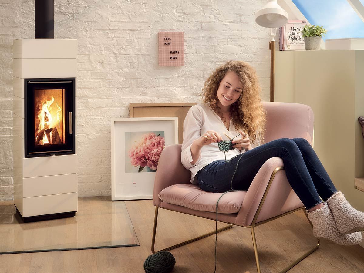 Femme se détendant dans un fauteuil rose près d'une cheminée allumée, tricotant dans un salon confortable.