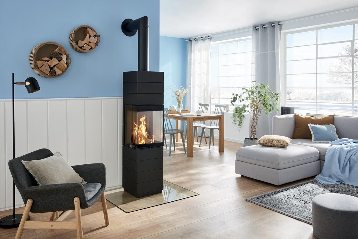 Salon moderne avec poêle à bois noir, mur d'accent bleu, grandes fenêtres et coin salon confortable.
