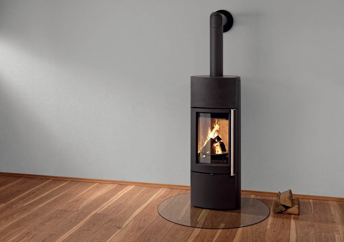 Poêle à bois noir avec un petit feu qui brûle dans une pièce minimaliste au sol en bois.