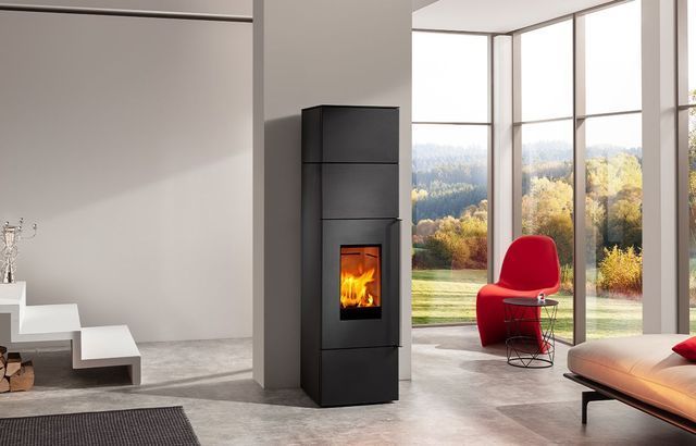 Salon moderne avec cheminée noire, fauteuil rouge et baies vitrées donnant sur les arbres.