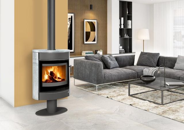 Salon moderne avec un poêle à bois noir, un canapé d'angle gris et une table basse en verre.