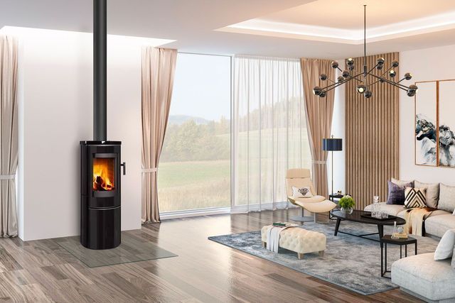 Salon moderne avec un poêle à bois noir, de grandes fenêtres, des rideaux beiges et un tapis à motifs bleus.