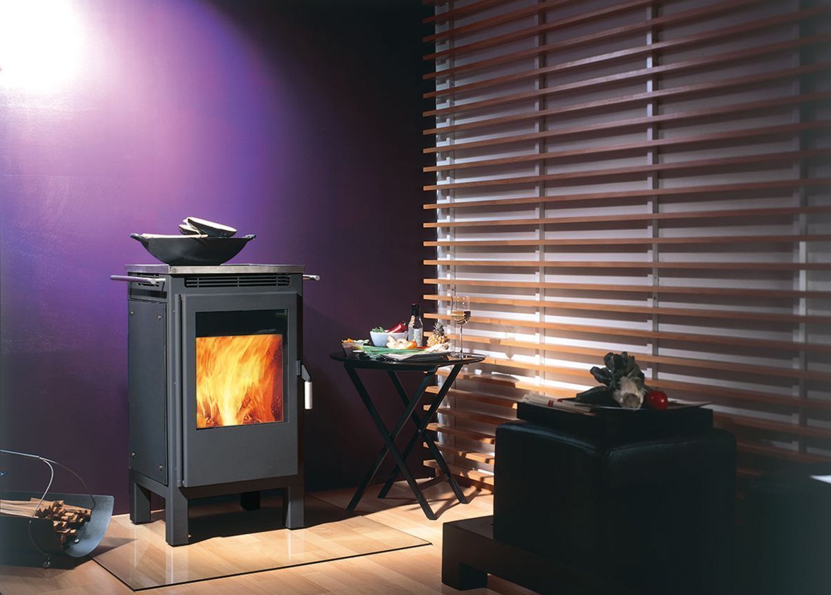Salon moderne avec un poêle à bois allumé, un mur violet et des stores en bois filtrant la lumière.