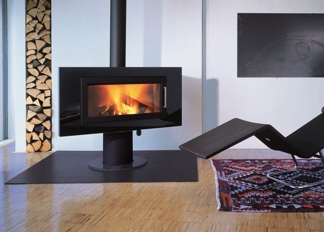 Salon moderne avec cheminée noire, bûches empilées, fauteuil et tapis coloré.