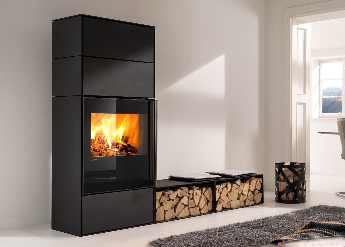 Poêle à bois moderne avec un feu qui brûle, à côté d'une pile de bois de chauffage dans un salon lumineux.