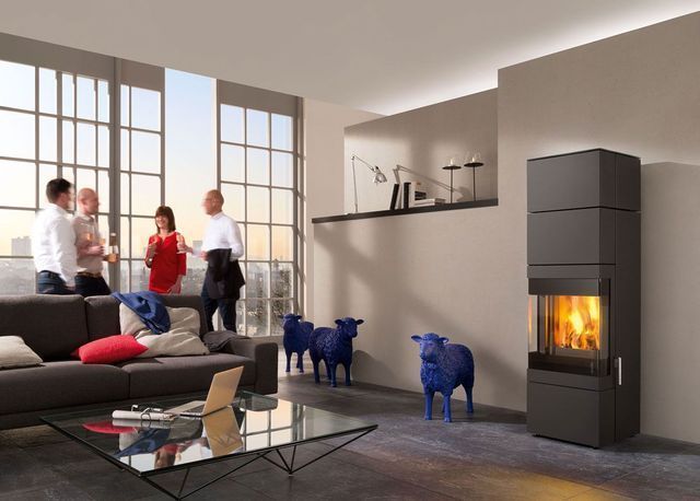 Salon moderne avec cheminée, fauteuils bleus et trois personnes près de grandes fenêtres.