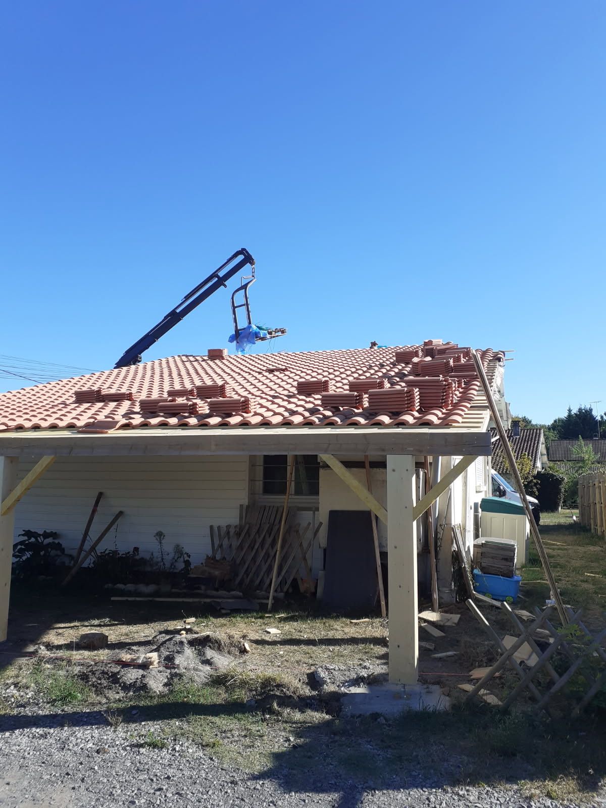 Toiture du carport en construction : tuiles rouges, grue, ciel bleu.