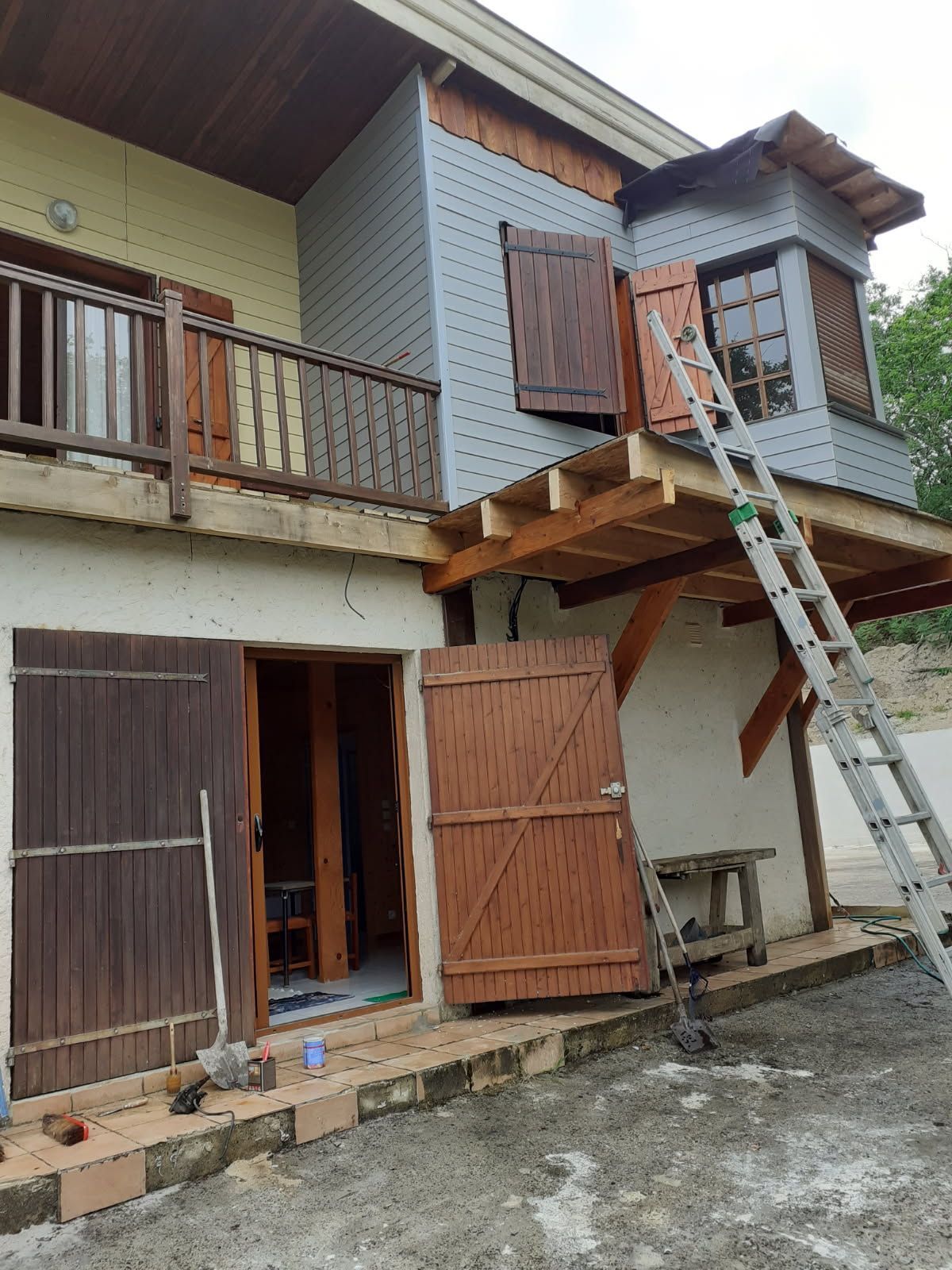 Extérieur de la maison en construction avec volets en bois, revêtement et échelle.