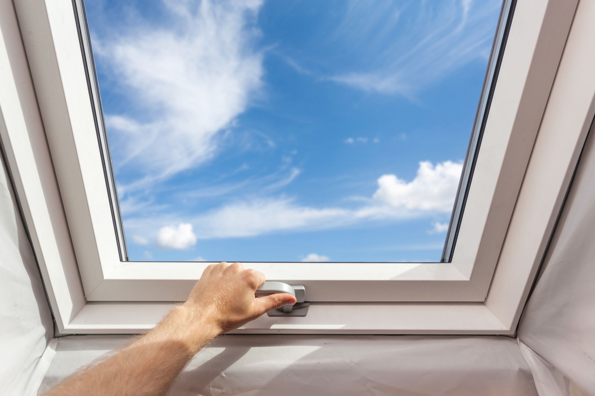 Main ouvrant une lucarne pour révéler un ciel bleu avec des nuages ​​​​filamenteux.