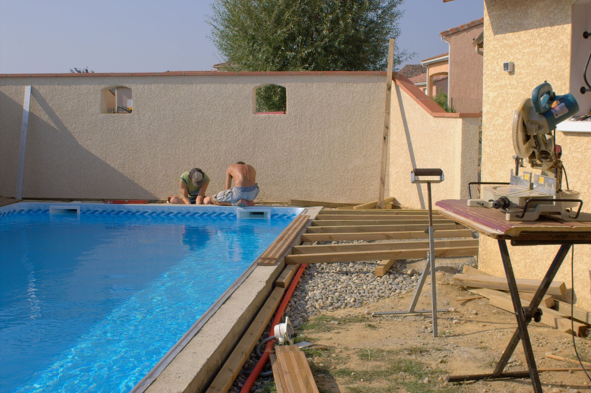 Deux hommes travaillant sur une terrasse près d'une piscine, avec une scie à onglet installée.