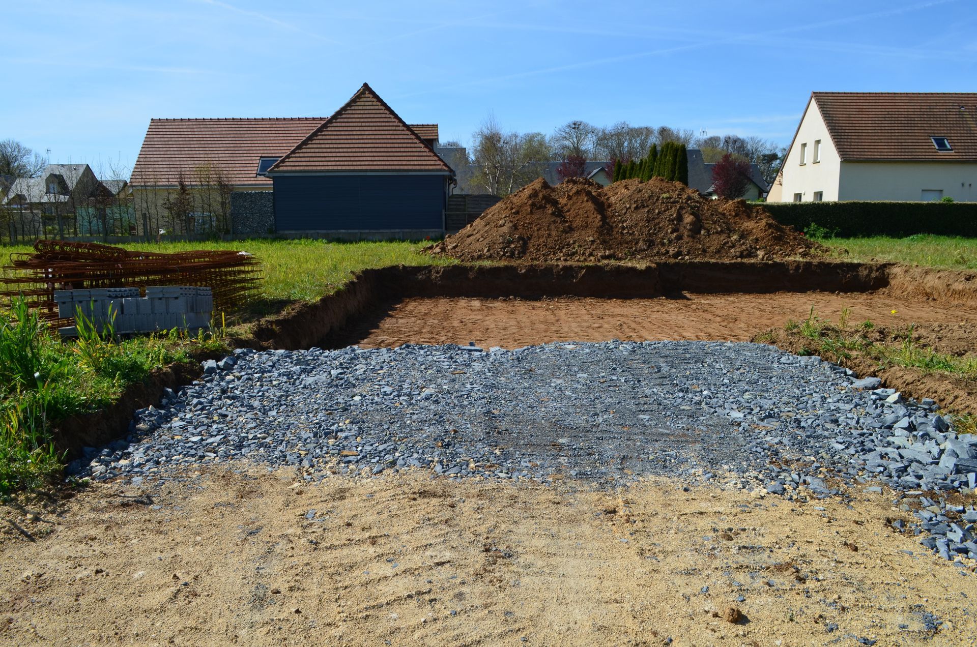Chantier de construction avec base de gravier et tas de terre devant les maisons.