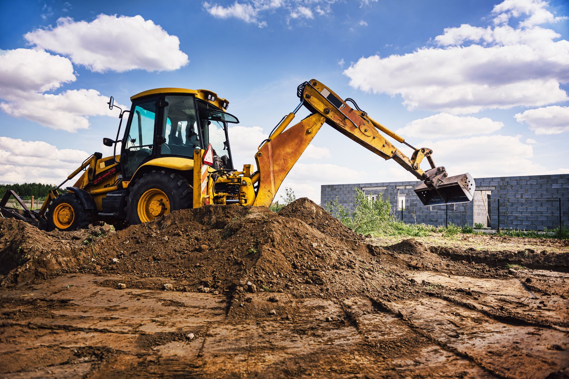 Une pelle rétrocaveuse jaune creuse dans la terre sur un chantier de construction sous un ciel bleu vif.