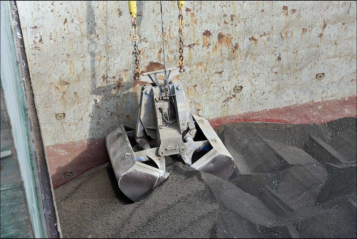 Un seau à benne preneuse récupère des matières grises à l'intérieur d'un récipient en métal.