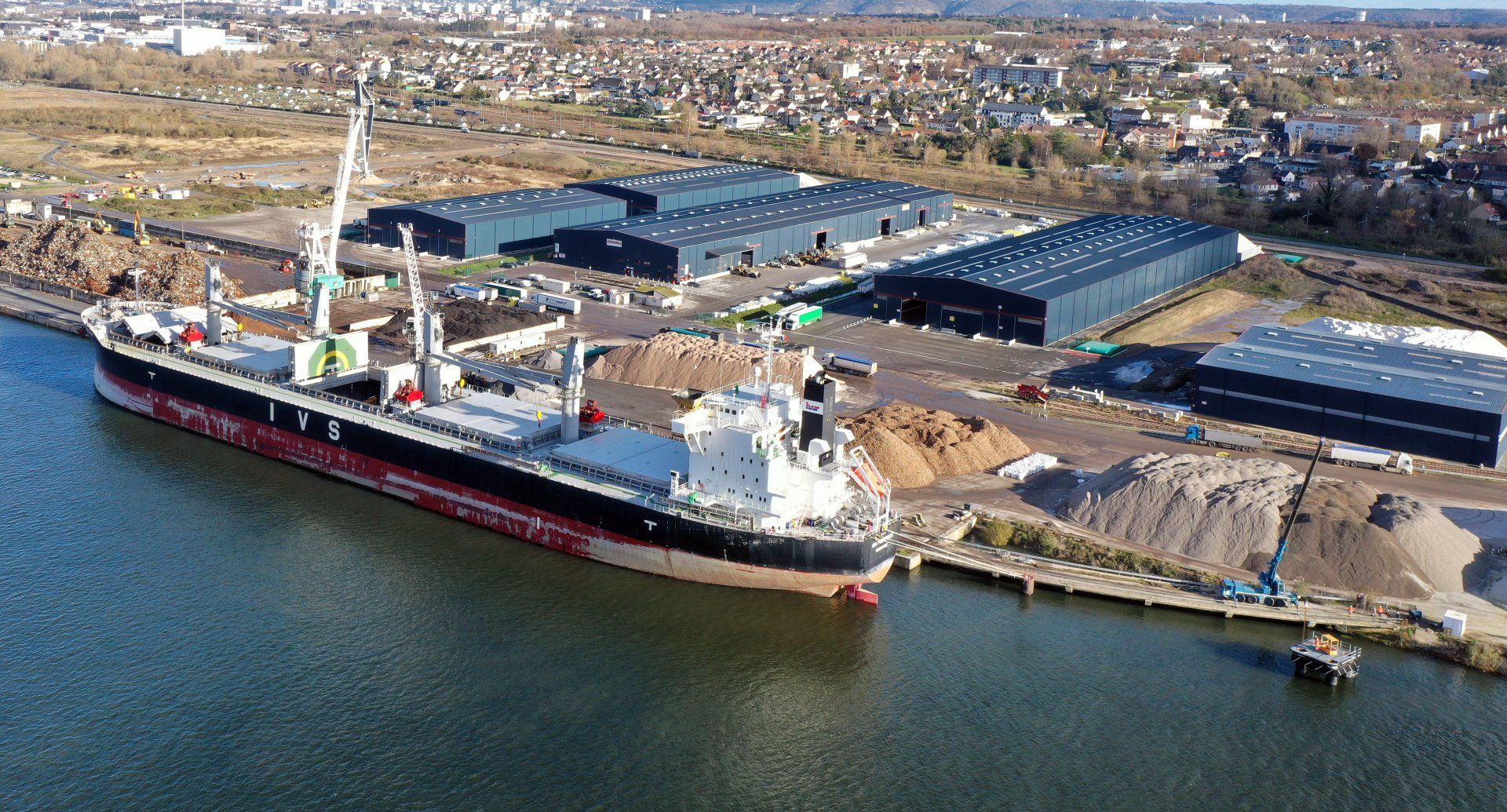 Grand cargo amarré dans un port avec des entrepôts en arrière-plan ; décor industriel.