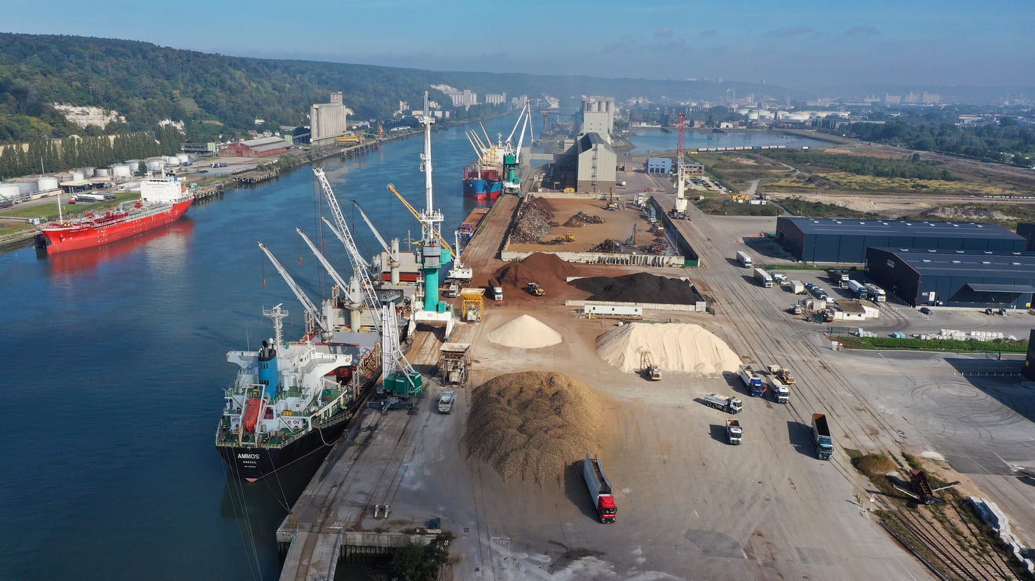 Vue aérienne d'un port animé avec des navires amarrés, des grues et des piles de marchandises.