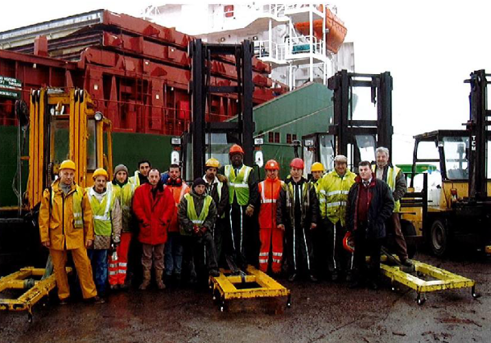 Un groupe de travailleurs portant des équipements de sécurité pose près de chariots élévateurs et de conteneurs d'expédition sur un quai.