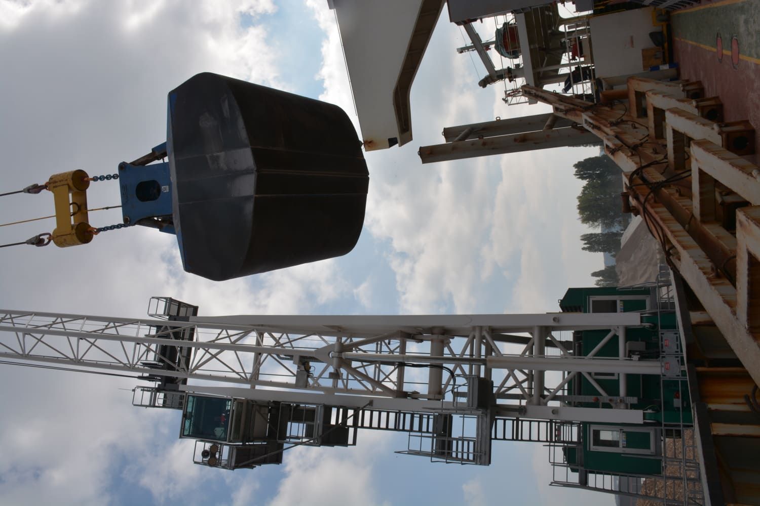 Grue soulevant un grand conteneur noir sur un navire, contre un ciel nuageux.