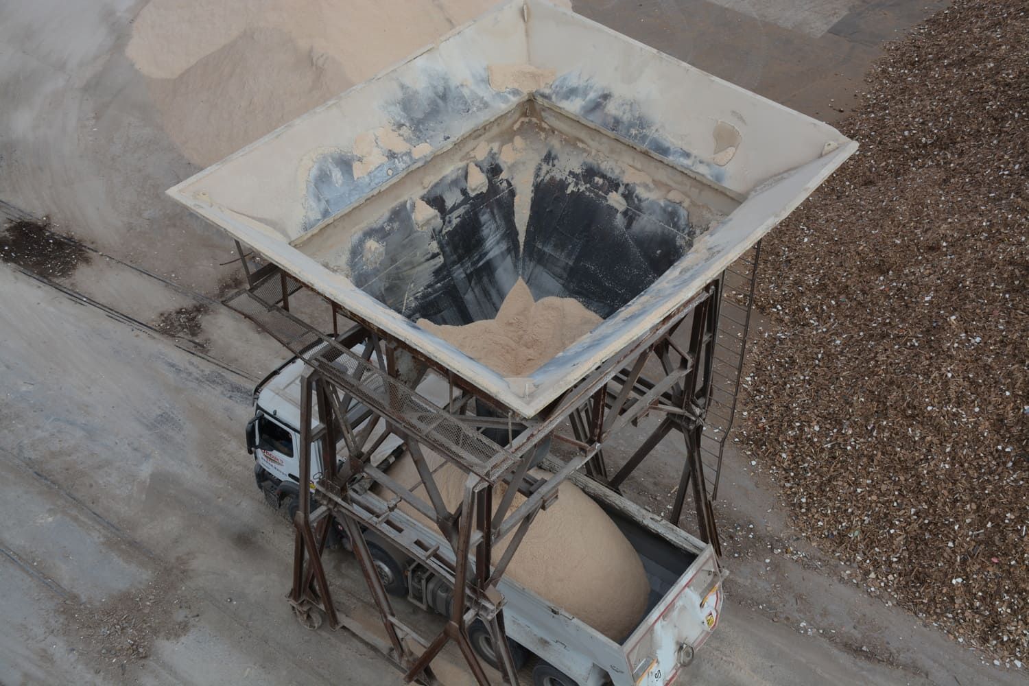 Une grande trémie industrielle distribuant du matériau dans une plate-forme de camion en dessous, à l'extérieur.