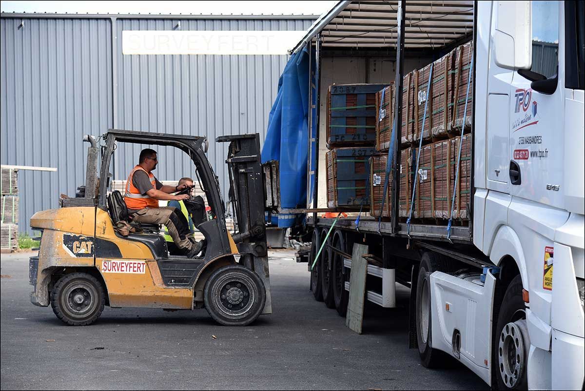 Opérateur de chariot élévateur chargeant des caisses dans un semi-remorque dans un entrepôt, en pleine lumière du jour.