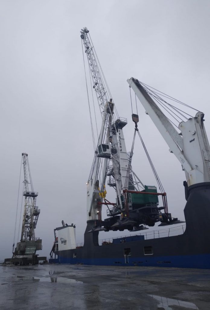 Un grand navire chargé de marchandises par plusieurs grues sur un quai sous un ciel nuageux.