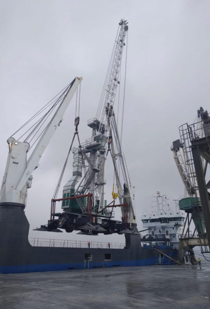Grues soulevant des machines d'un navire dans un port par temps nuageux.